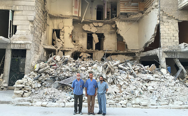 Kahler, Sahloul and Attar in front of a building destroyed by a barrel bomb.