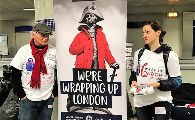Hands On London volunteers promote the annual Wrap Up London coat drive at a Tube station, with a poster of Napoleon Bonaparte in a bright red, fur-trimmed coat.