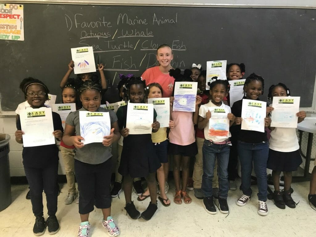 Brittany Turner (center) explains the dangers of proposed seismic blasting in the ocean to third-graders at a local Boys and Girls Club and helps them write letters to North Carolina Gov. Roy Cooper./ Courtesy Brittany Turner