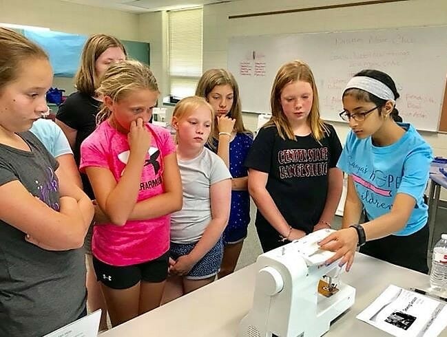 Sanya Pirani (far right) teaches students at Hidden Oaks Middle School in Prior Lake, Minn., how to sew in hopes that they will join her in sewing bags to be filled with items for children in need/ Courtesy Sanya Pirani