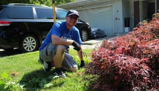 Man in a blue shirt kneels in a yard while gardening.