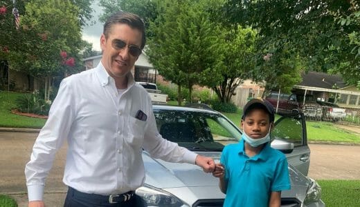 Smiling man and boy fist bump while standing in a driveway.