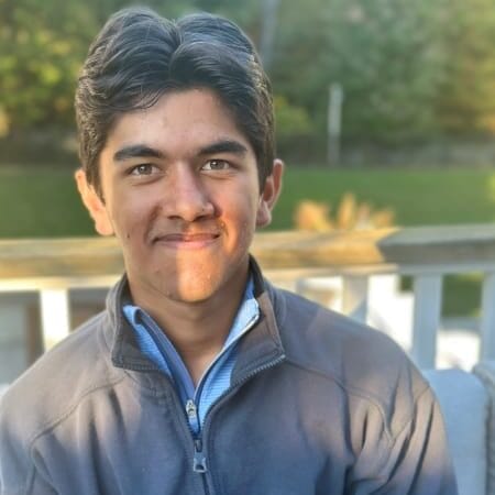 Young person in a button up shirt and jacket smiles directly at the camera.