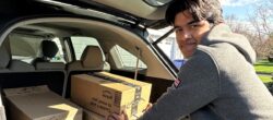 Young person loads several cardboard boxes into the back of a car.