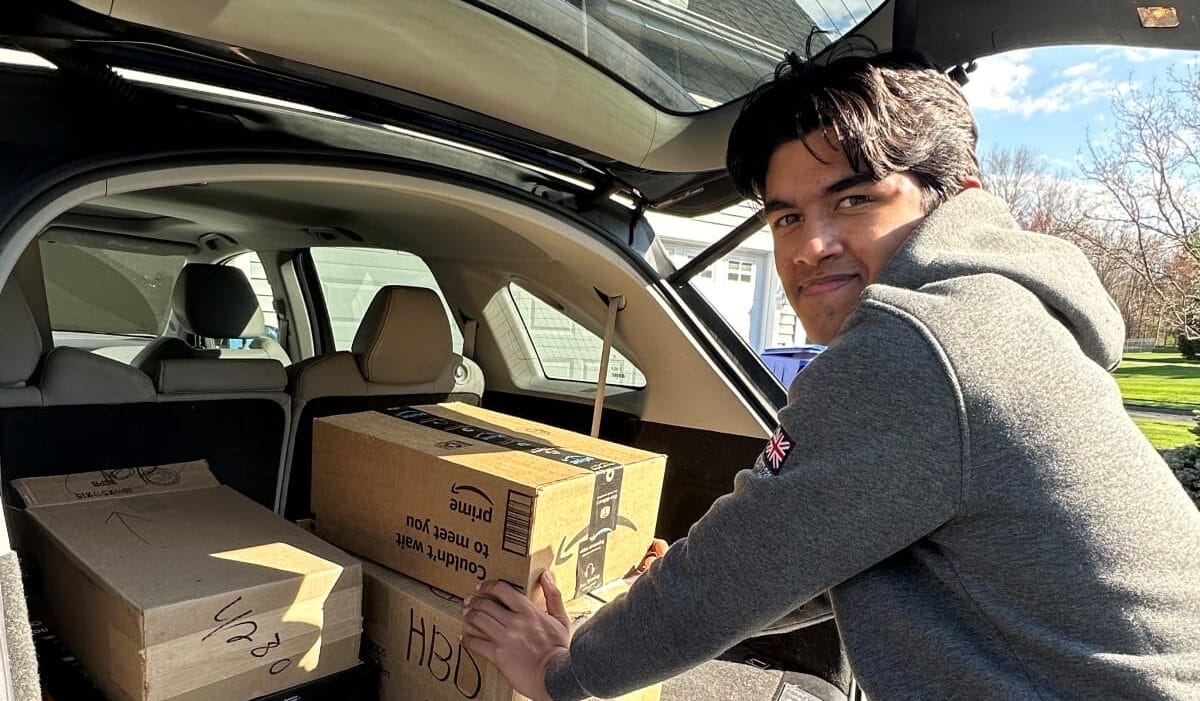 Young person loads several cardboard boxes into the back of a car.